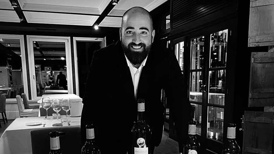 Profesional en un comedor de restaurante, con botellas de vino sobre la mesa, en una fotografía de archivo en blanco y negro.